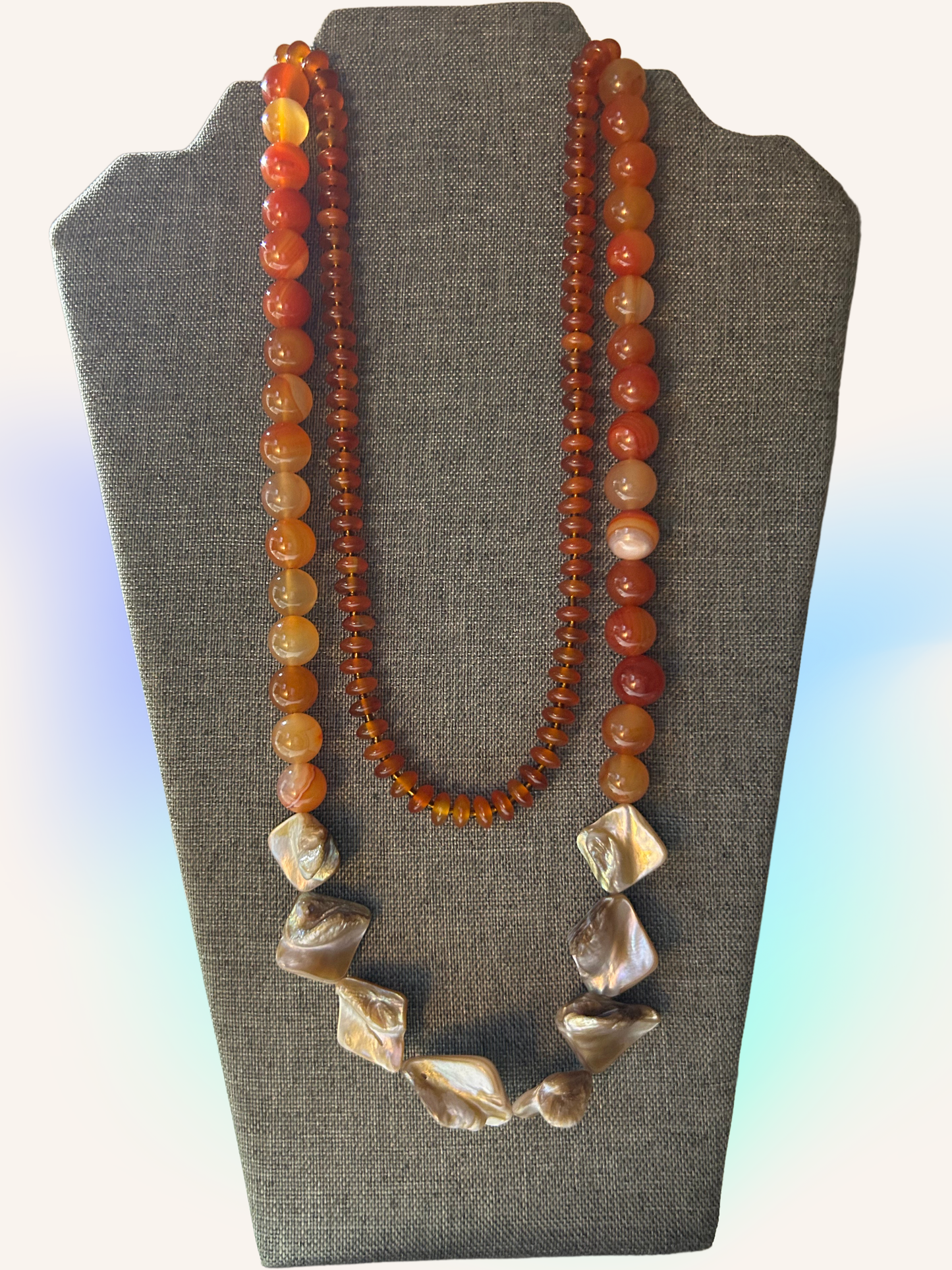 Necklace with amber and shell beads on a gray stand